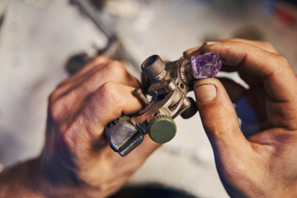 Two hands working on a piece of amethyst stone